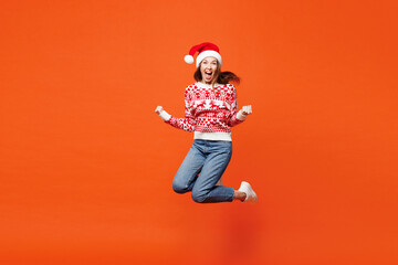 Full body merry young surprised shocked woman wear red Christmas sweater Santa hat posing jump high...