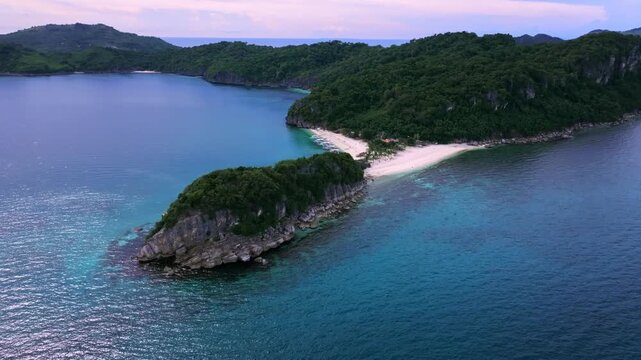 Aerial view of islands converging to form a beach contrasting with turquoise waters and lush green trees, Carles, Western Visayas, Philippines.