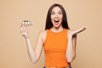 Young shocked surprised woman wear orange casual clothes hold eat look at piece of cake isolated on...