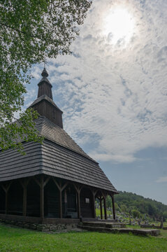 View of a rustic wooden church standing proudly under a sky filled with fluffy clouds, its dark timbers contrasting against the bright, sunlit sky, Topola, Presovsky kraj, Slovakia.