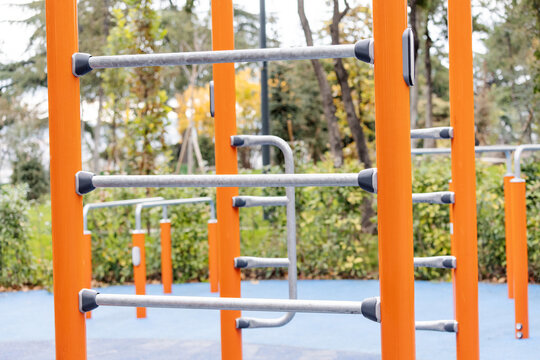 Modern outdoor gym equipment featuring orange columns and metal bars for calisthenics and bodyweight exercises in a public park