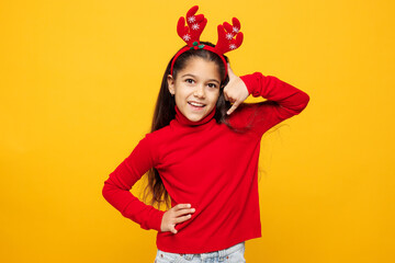 Merry little girl wear red clothes fun decorative deer horns on head posing do phone gesture says call me back isolated on plain yellow background Happy New Year Christmas celebration holiday concept