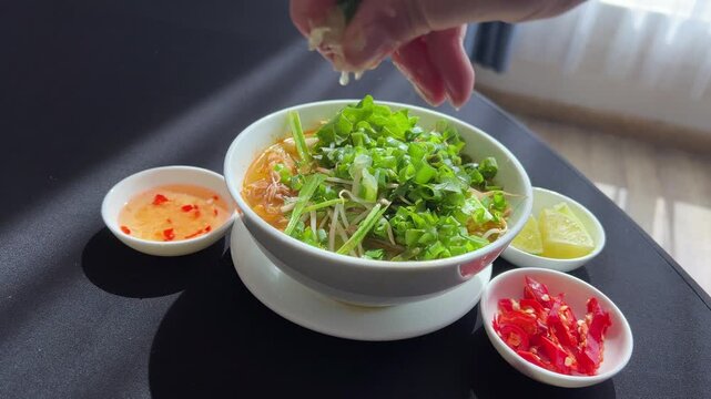 Chef garnishing encebollado con yuca traditional ecuadorian soup. squeeze lemon juice into pho bo soup, a traditional Vietnamese soup.