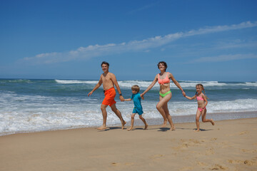Family with kids enjoy lively run on the sunny beach together