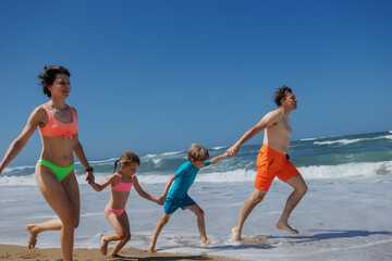 Young parents and kids happily running on the sandy sea shore