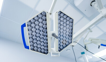 Modern surgical lights in operating room ceiling. Dual hexagonal LED operating lamps with blue handle hanging from the ceiling in a sterile hospital theater.