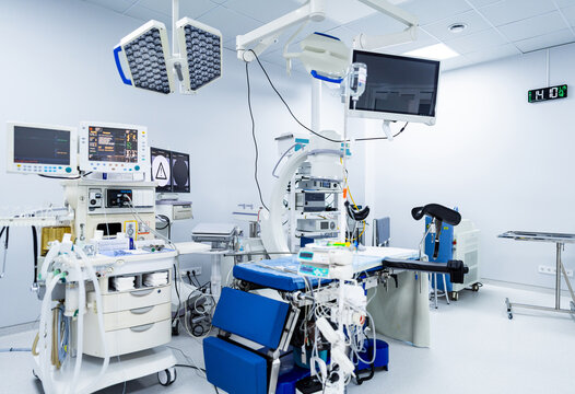 Fully equipped modern operating room interior. Advanced surgical theater with C-arm, monitors, operating table and overhead lights ready for procedure.