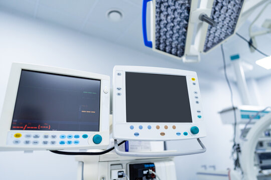 Dual Medical Monitors in Modern Operating Theater. Two digital medical monitors suspended on an articulating arm displaying vital data in a sterile hospital operating room environment. - Powered by Adobe