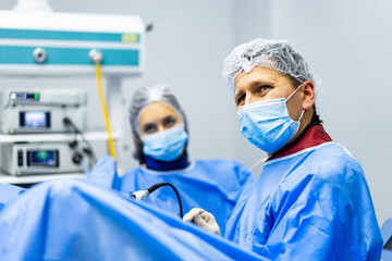Surgical Team Performing Laparoscopic Operation in Clinic. Male surgeon and female assistant performing a medical procedure using high-tech laparoscopic equipment in a modern operating theater.