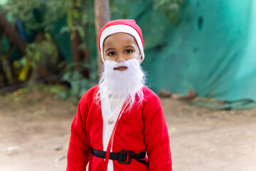 little boy in santa claus outfit with white beard outdoors