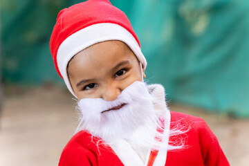 little boy cute smiling facial expression in santa claus outfit with white beard outdoors