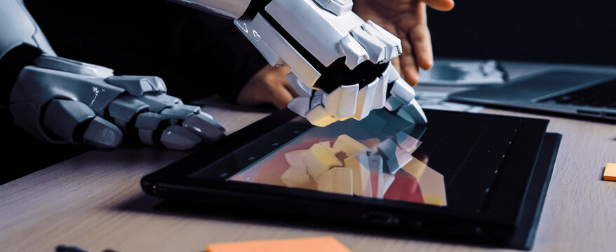 A robot hand interacts with a touchscreen tablet in a modern workspace, showcasing the blend of artificial intelligence and human creativity in design and collaboration.Noogenesis