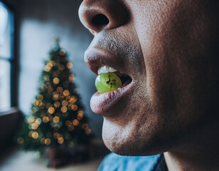 Man eating a green grape on New Year&rsquo;s Eve with blurred Christmas tree lights