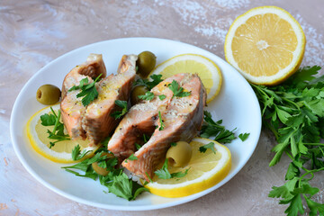 Cooked Salmon Steaks decorated with Lemon, Parsley and green Olives on a White Plate