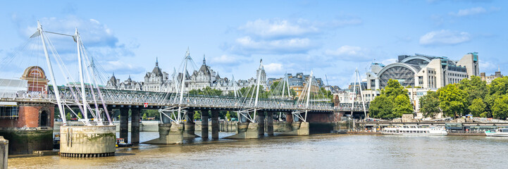 A panoramic riverside view of the Golden Jubilee Bridges and Charing Cross station in the City of London along the north bank of the Thames