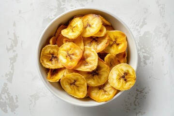 Golden brown fried plantain chips in a white ceramic bowl on a marble surface