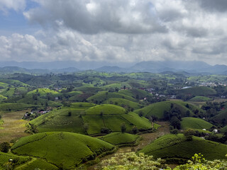 View of verdant green hills cascade under a sky streaked with dramatic clouds, creating a serene yet vibrant landscape, Phu Tho, Phú Thọ, Vietnam.