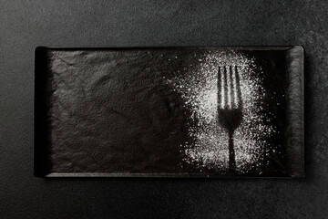 Imprint of a fork with powdered sugar on a black rectangular plate