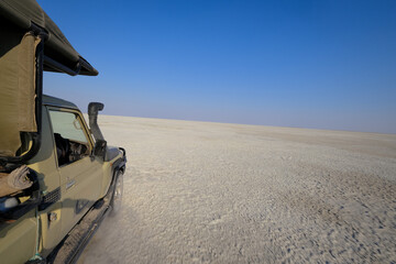 Safari vehicle driving across the Makgadikgadi Pan in Botswana. Adventure travel scene on a vast white salt flat under a deep blue sky in southern Africa.