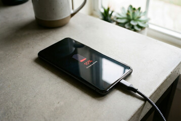 Smartphone charging with low battery indicator on modern concrete table, technology and daily lifestyle scene with indoor natural light by window