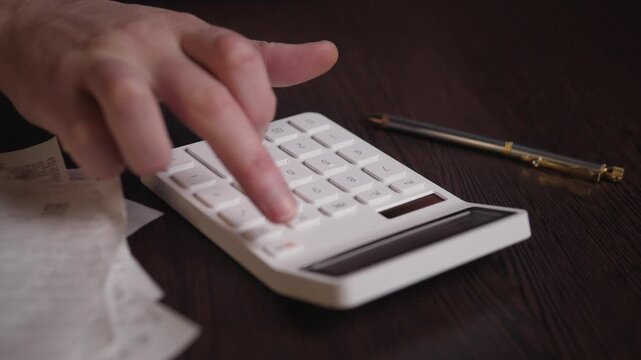 Finger Tapping Calculator Near Receipts, Retail Proprietor Checking Daily Totals With Pen Beside Device, Neat Receipt Pile And Dark Desk Surface, Evening Sales Reconciliation, Focused