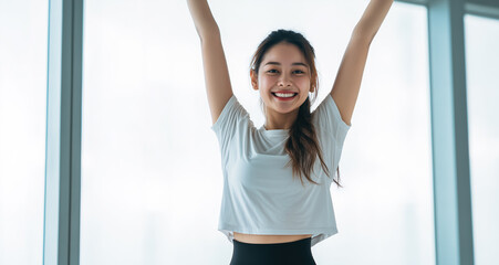 Smiling woman with arms raised in a bright indoor space during a fitness routine in the morning light