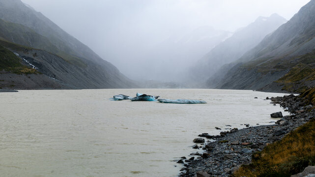 View of milky waters reflecting the looming mountains, with scattered icebergs adding a touch of surreal beauty, Hooker Lake, Canterbury Region, New Zealand.