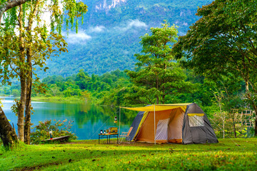 Camping tent on green grass in the morning, antique gas lamps, retro chairs, with outdoor coffee-making facilities on tables in a forest camping area.