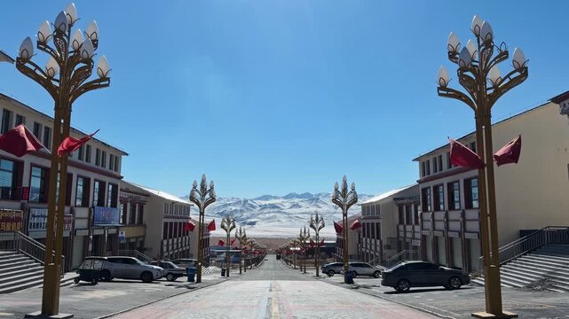 Qilian Grassland, Xining, Qinghai Province, China - A Wide, Symmetrical Street Lined with Ornate Lampposts and Buildings Leads Toward Snow-covered Mountains Beneath a Clear Blue Sky - Static Shot