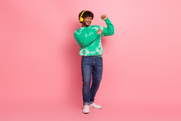 Young man dancing in a green tie dye sweater wearing headphones against a pink background for a...