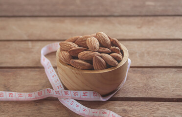 Almonds in a wooden cup on a wood plate with a measuring tape, symbolizing healthy diet control.
