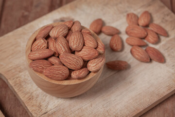 Almonds placed in a wooden cup and on a natural wood plate, highlighting simple organic textures.