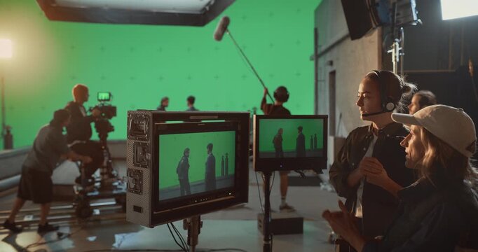 Backstage on a Professional Film Set, Director and Crew Supervise Actors Performing an Scene Before a Large Green Screen, Video Monitors to Capture Cinematic Footage for Visual Effects Production.