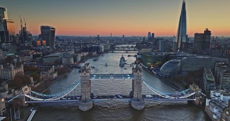 Aerial view Tower Bridge glowing over River Thames at sunset, evening traffic and boats framed by historic landmarks and modern skyscrapers. The Shard and Gherkin night cityscape. Drone flight footage - Powered by Adobe