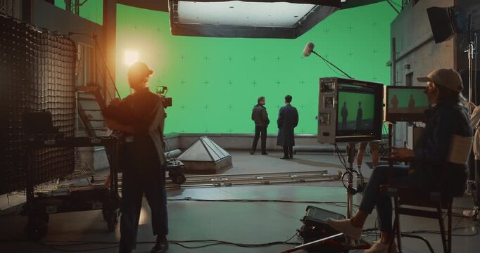 Behind the Scenes on a Busy Movie Set, Film Crew Operates Camera Dolly, Actors Perform a Dramatic Scene Against a Large Green Screen, Capturing Cinematic Footage. Wide Shot