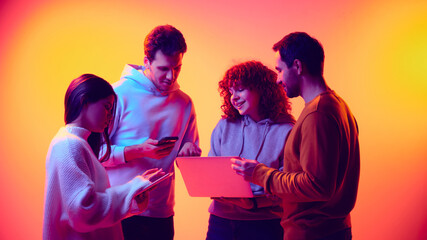 Business team collaborating across digital devices in neon light. Concept of shared data access, cross platform workflow, digital collaboration, mobile tools and flexible business processes.