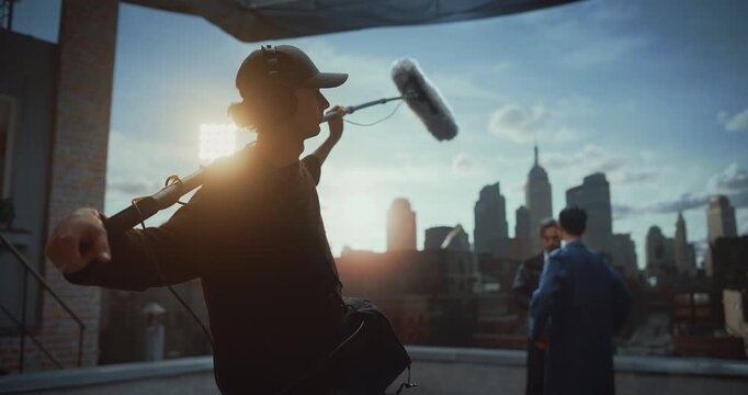 Professional Soundman Operates Boom Microphone While Two Actors Perform Dialogue on Movie Set Rooftop, Capturing Production Audio During Dramatic Film Scene in Studio Cinematic Storytelling