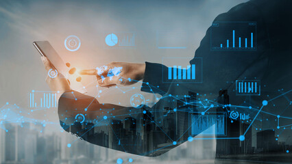 A business person interacts with a smartphone displaying digital graphs and charts, symbolizing the intersection of technology, data, and urban growth at sunset. Xenic