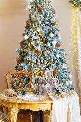 Fully decorated Christmas tree with golden and white ornaments, table with dough and rolling pin for baking holiday gingerbread cookies. Cozy festive aesthetic kitchen interior, winter holiday mood