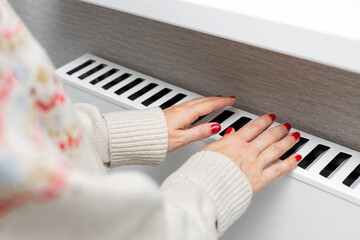 A woman warms her hands by holding them over a radiator. a woman warms her hands at home. A girl warms herself near a heating radiator. person warming up. thermal energy. cold season. utility bills. h