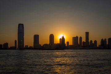 A view during sunset on the Hudson River and the setting sun between the buildings of the skyline of Jersey City, New York, USA
