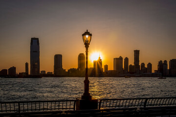 A view of the Hudson River and the setting sun between the old lantern and the buildings of the skyline of Jersey City, New York, USA
