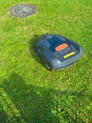 Fototapeta premium Robotic lawn mower navigates a sunny backyard on a bright afternoon while keeping grass neatly trimmed around a manhole cover