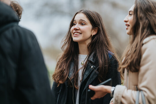 Teenage friends chat and smile outdoors in a candid, natural moment. The scene shows teenagers in jackets conversing outside, capturing friendship and youth.