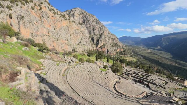 Delphi temple 4k video. Panoramic view of the ancient Greek theater of Delphi built into the rocky mountainside, overlooking a deep green valley under a clear blue sky.