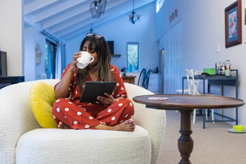 Indian woman drinking coffee and using tablet at home