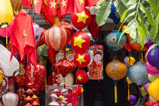 View of vibrant red flags and lanterns with yellow stars create a festive display, juxtaposed against the dark backdrop of a bustling market, Hanoi, Hanoi, Vietnam.