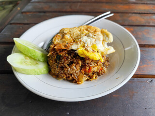 Fried rice with egg and vegetables in a white plate, at an outdoor stall during the day.