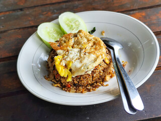 Fried rice with egg and vegetables in a white plate, at an outdoor stall during the day.