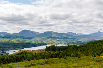 Obraz premium Isle of Skye, Scotland - Rolling hills, lake view, and forested mountains under cloudy sky – a serene nature landscape